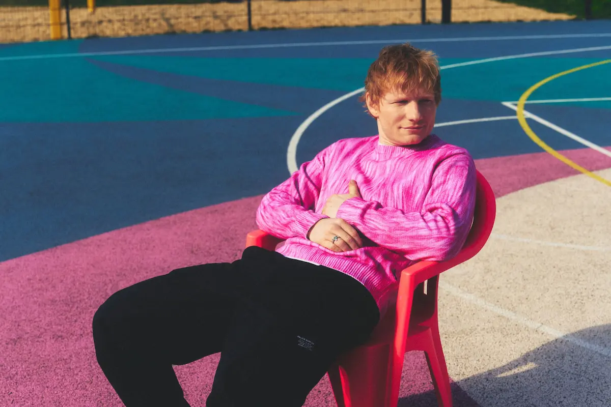 Ed Sheeran Konzert 2025 München Ticket-Verkauf - hier ein Pressefoto von Ed Sheeran 2025. bei dem der Künstler auf einem Stuhl in einem Stadion bzw. auf einem Sportplatz sitzt