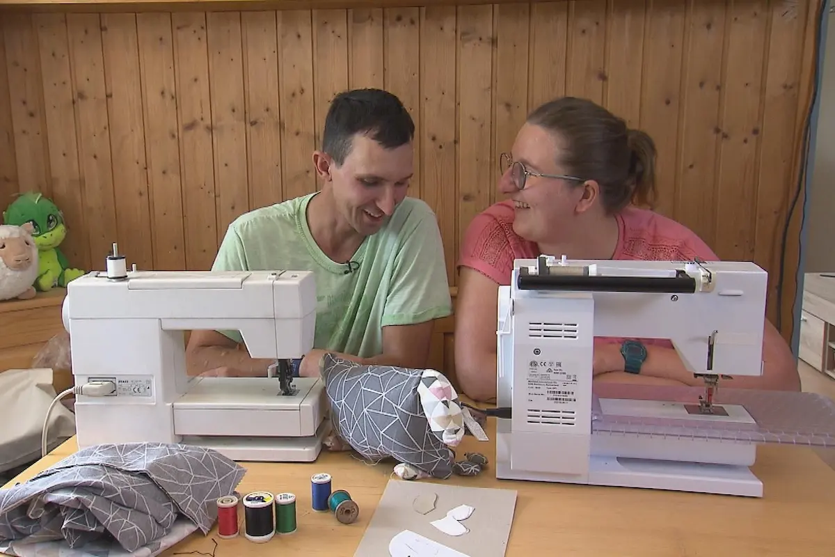 Michael und Julia sitzen nebeneinander an ihren Nähmaschinen und konzentrieren sich auf ihre Handarbeit. Während sie gemeinsam kleine Plüsch-Schafe nähen, herrscht eine gelöste Stimmung. Michael genießt die Zweisamkeit mit Julia, auch wenn er betont, dass er Zeit braucht, um sich emotional vollkommen zu öffnen.