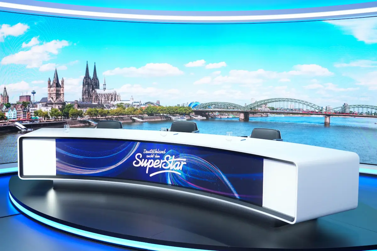Das Jury-Pult bei DSDS 2026 - zu sehen im Bild ist das bekannte, weiße DSDS-Jury-Pult mit dem Logo der Casting-Show vorn; im Hintergrund zu sehen ist ein Oanorama-Bild von Köln mit Blick über den Rhein auf die Hohenzollernbrücke und den Kölner Dom