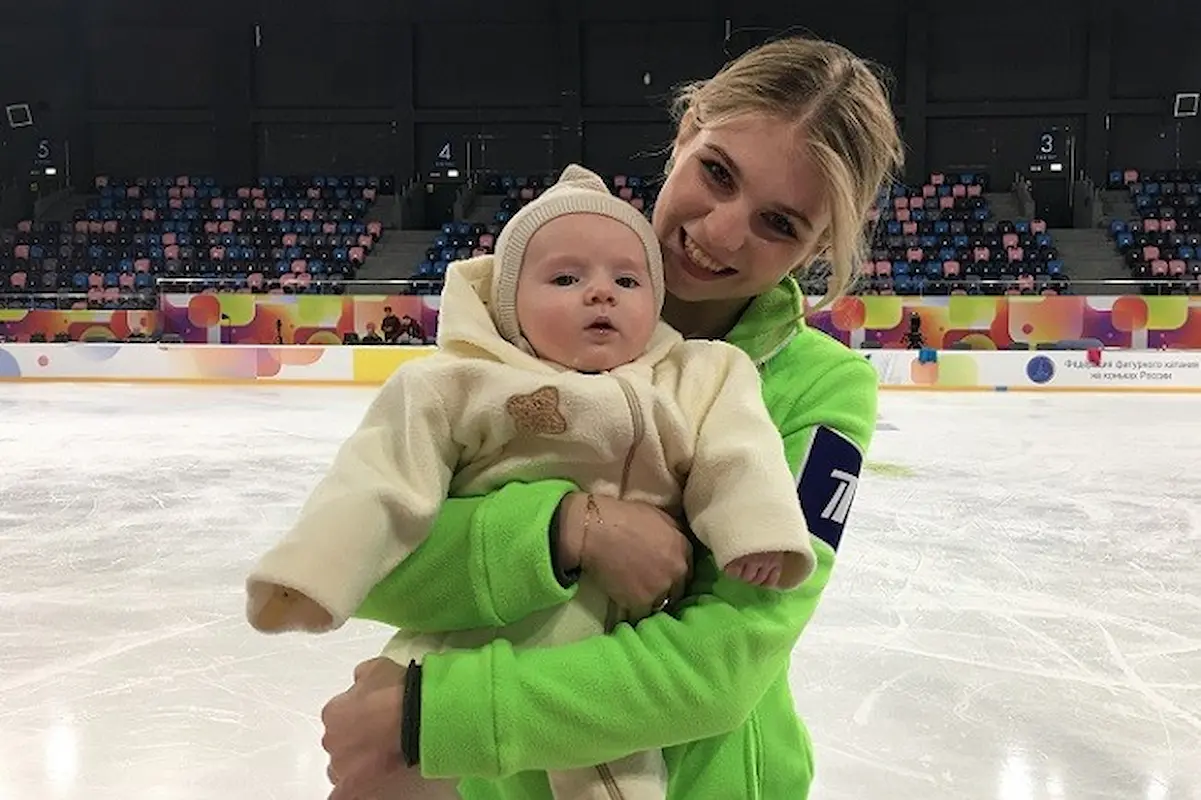 Eiskunstlauf: Kamila Valieva und Alexandra Ignatova (Trusova) sind zurück - hier im Bild Alexandra Trusova (Ignatova) mit ihrem Sohn Misha am Rande des Geschehens beim Team-Wettbewerb in Kaluga; Sascha (Alexandra) steht auf dem Eis, hält ihr Baby in den Armen und lacht in die Kamera 