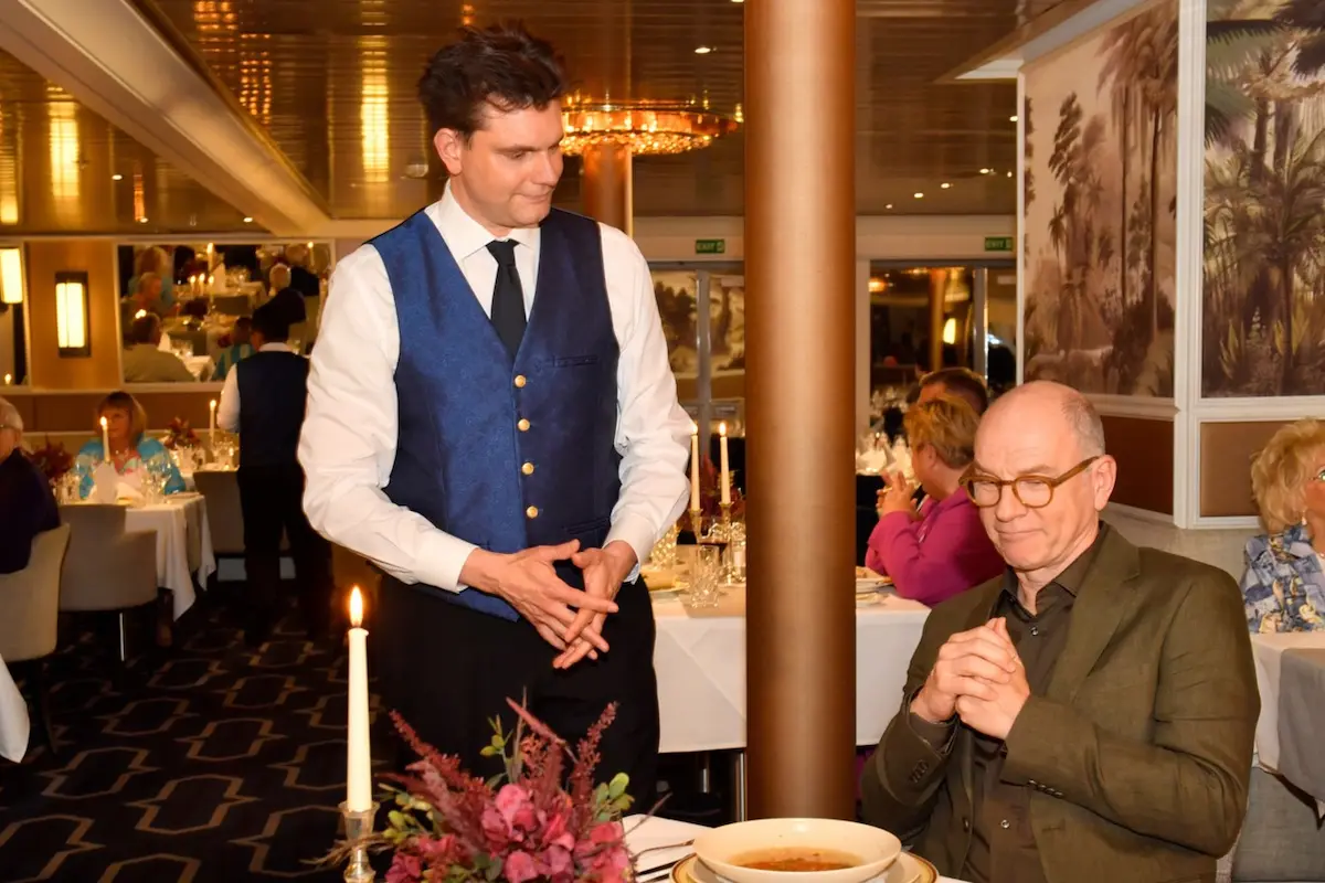 Kellner Peter (Lutz van der Horst) und Oliver Stiller (Götz Schubert) - Szene-Foto vom Traumschiff Neujahr 2026, bei der der Kellner seinen Gast bedient