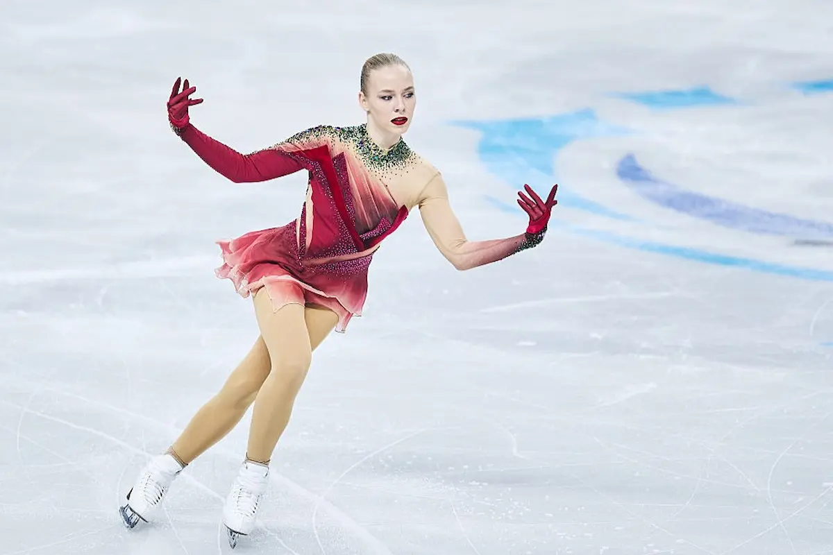 Niina Petrokina aus Estland bei der Eiskunstlauf-EM 2026 in Sheffield, Kurzprogramm - das Bild zeigt Niina Petrokina auf dem Eis bei ihrem Kurzprogramm, sie trägt ein rotes Kleid mit langen, über die Arme reichende Handschuhen, die direkt am Kleid angenäht sind