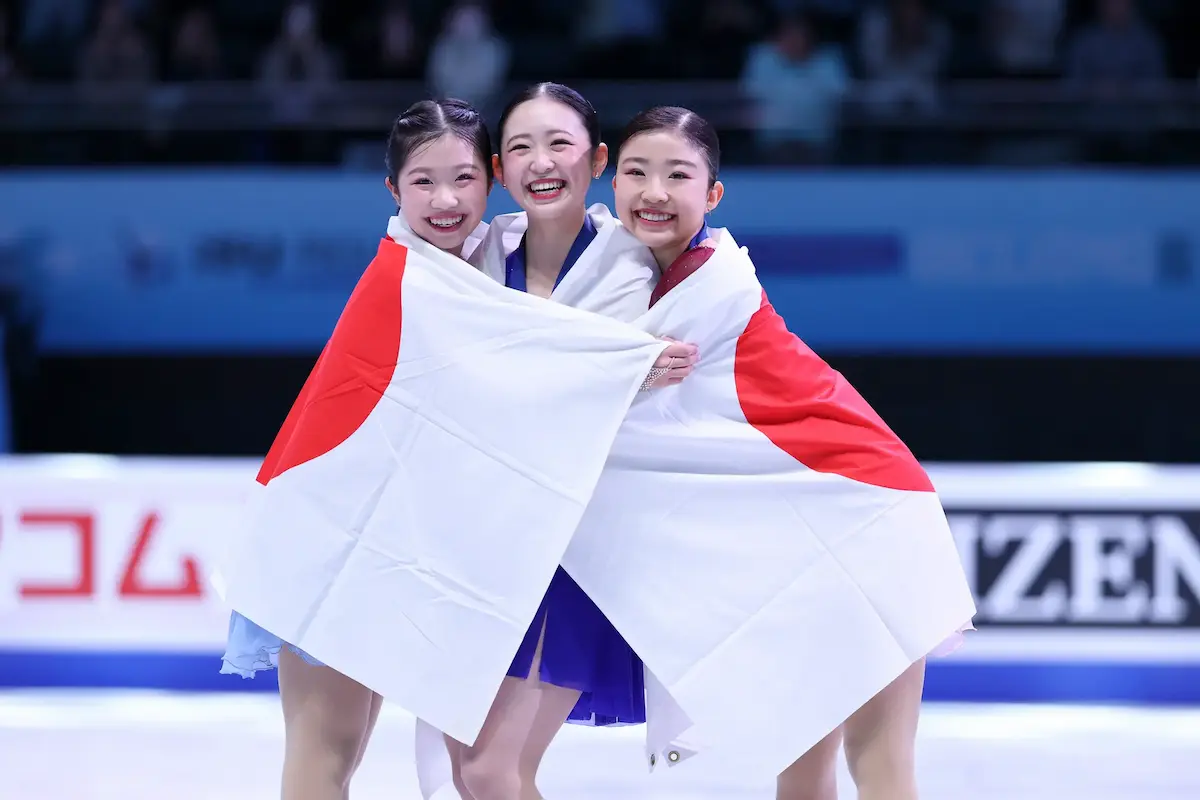 Siegerehrung Eiskunstlauf-Frauen 4 Continents 2026 - hier im Bild Ami Naki, Yuna Aoki und Mone Chiba - alle aus Japan - die drei jungen Eiskusntläuferinnen stehen dicht beisammen, lachen in die Kamera und hüllen sich gemeinsam in eine japanische Flagge