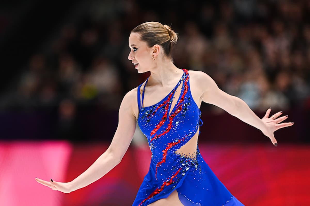 Kamila Valieva 2026 im Kurzprogramm - sie trägt ein blaues, besetzt mit Glitzersteinen und roten Stoffstreifen, die aussehen wie Flammen 
