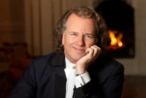 Andre Rieu Konzerte 2027 - Städte, Termine, Orte, Ticket-Tipps - auf dem Foto ist der Künstler zu sehen, der seinen Kopf in eine Hand stützt und in die Kamera lächelt