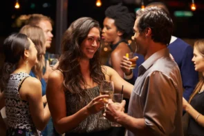 Ist ein Schnuppertanzkurs beim ersten Date eine gute Idee? Ja! - hier im Bild zu sehen ist ein Pärchen in einer Bar, das sich anlächelt - direkt hinter dem Pärchen steht eine Gruppe weiterer Gäste, die sich unterhalten